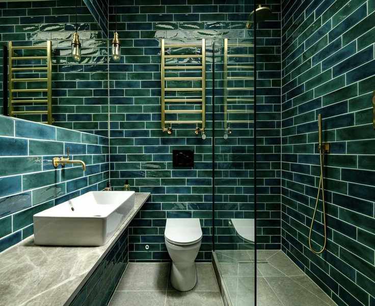 A green bathroom with green wall tiles and brass fixtures and fittings and a glass shower door