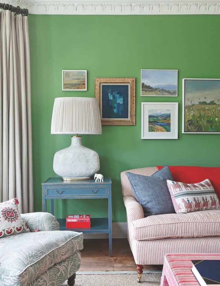 Green living room with gallery wall striped red and white sofa and a blue side table with a large lamp
