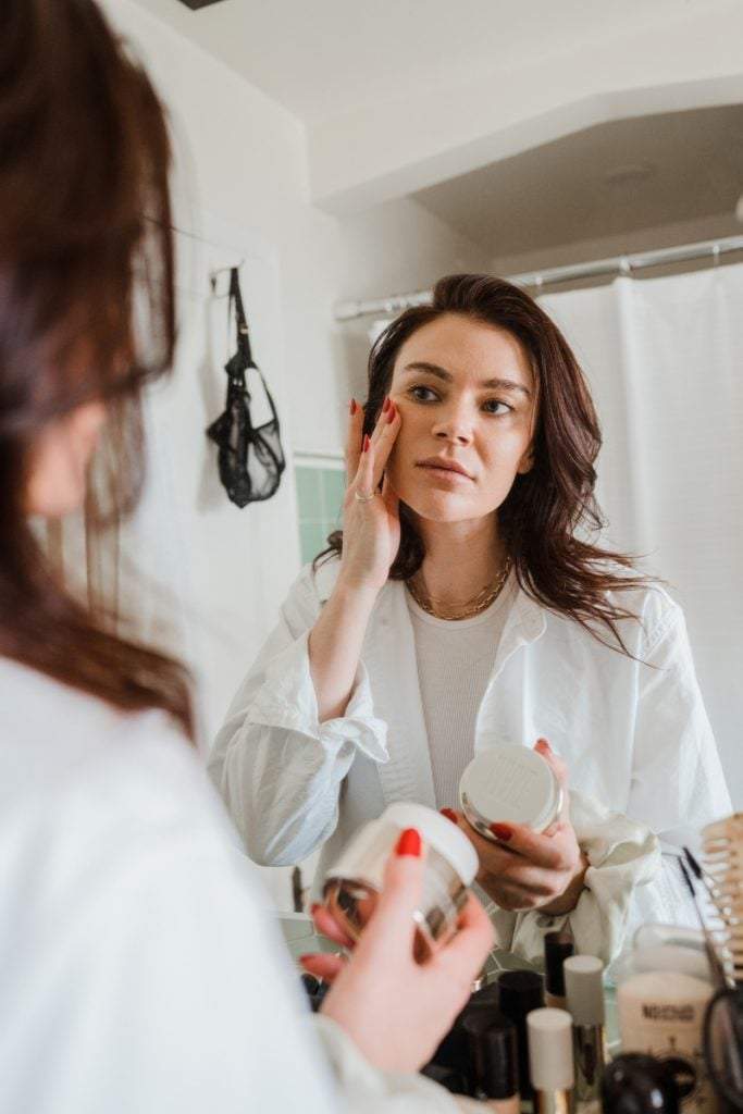 woman applying skincare at bathroom mirror_how to hydrate skin