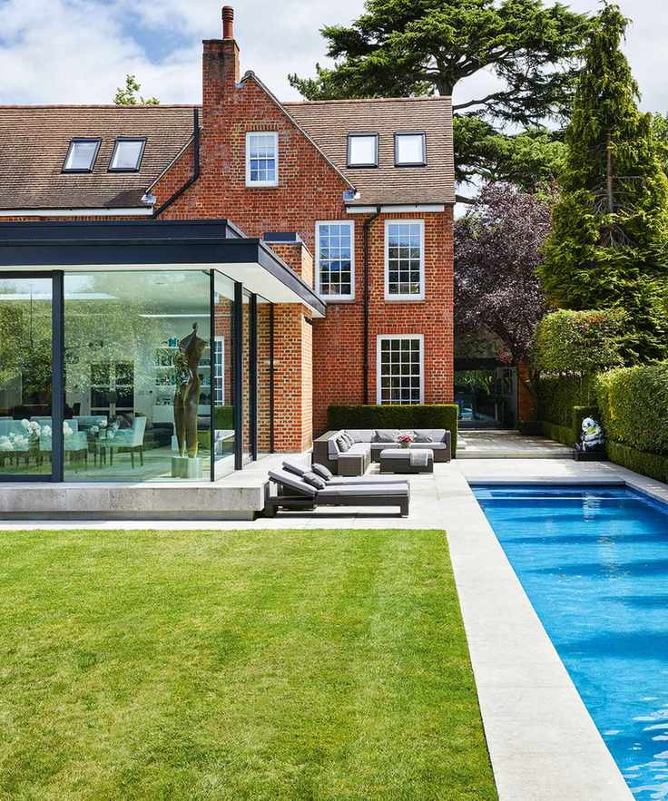A narrow swimming pool next to sun loungers and a large house