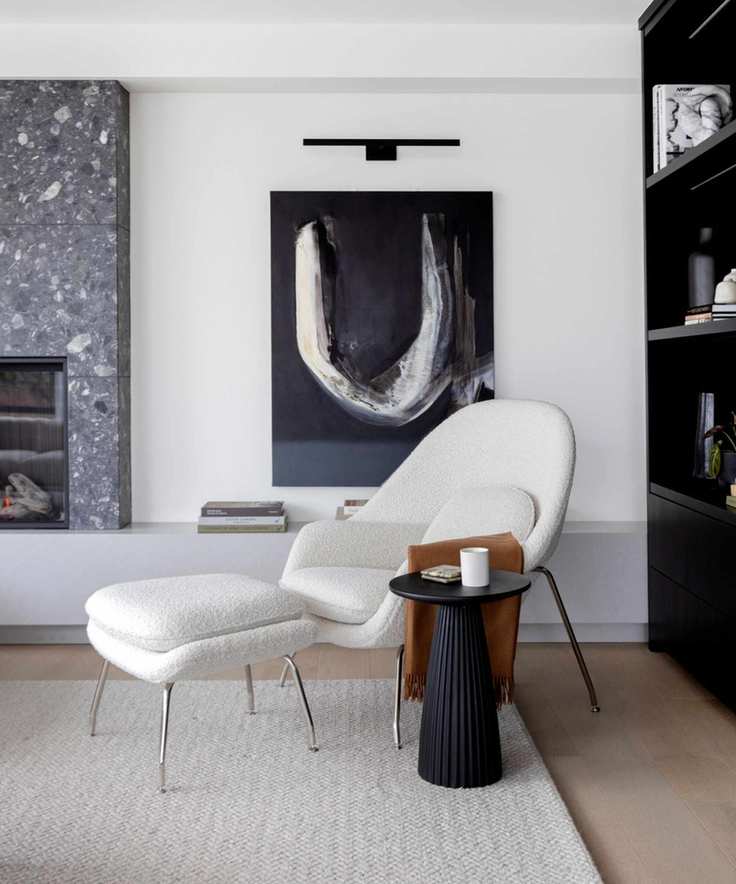 living room with a white boucle mid-century modern style chair and footrest with a large piece of black artwork on the wall behind
