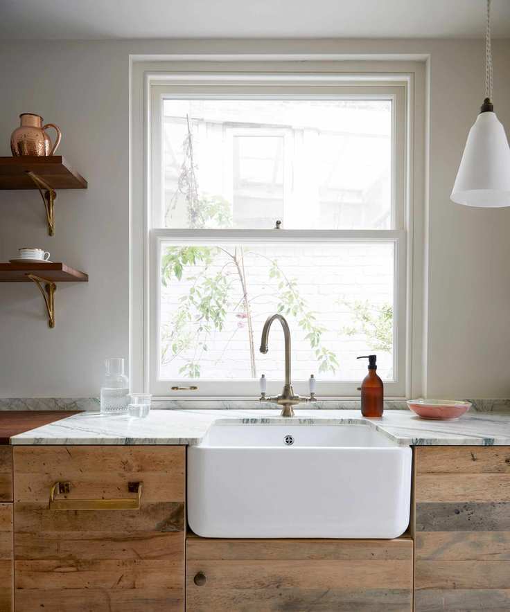 Calming contemporary kitchen with wooden plank kitchen cabinets, white sink, large window, hanging pendant light beside window, shelving beside window
