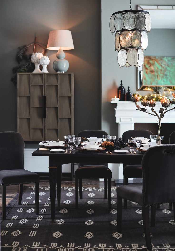 dining room with grey walls, fireplace, tallboy, table lamp, pendant light, black table, grey upholstered chairs, black rug