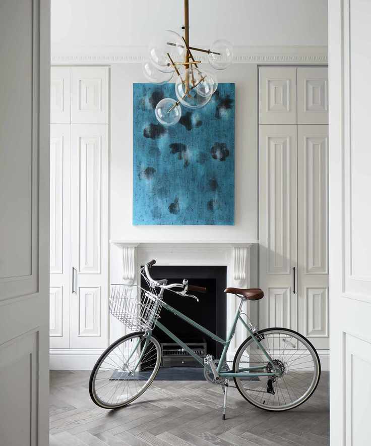 A white entrance hall with floor-to-ceiling storage cupboards and large blue artwork over the fireplace