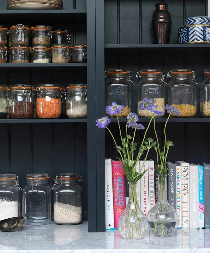 A close up shot of black open shelving storing food jars, books, and flowers