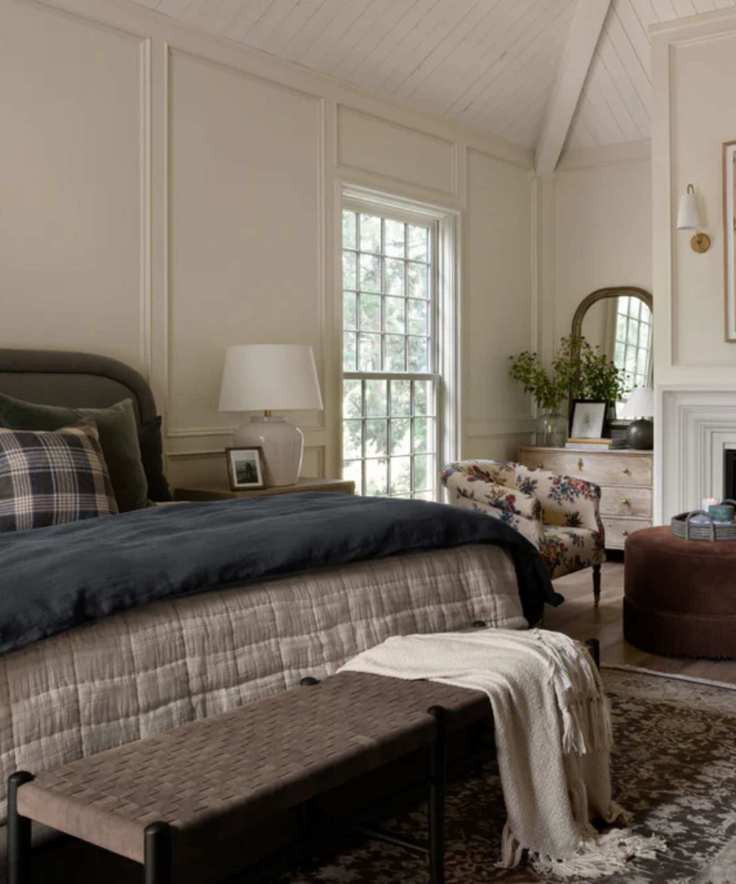 neutral panelled vaulted ceiling bedroom with a dark green bed, navy and plaid linens and a seating area