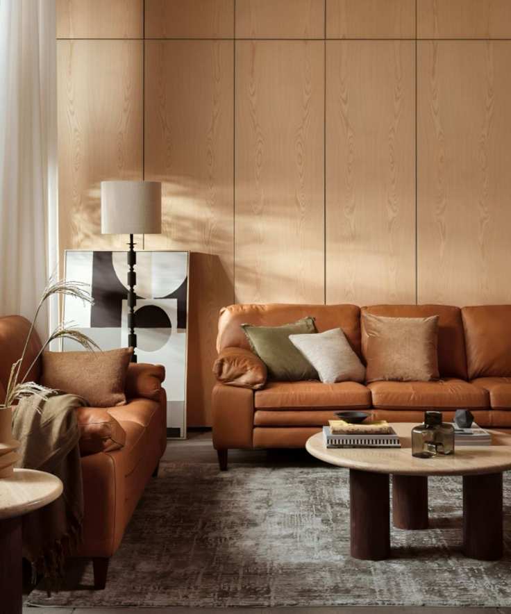 A living room featuring wood paneling, two brown leather sofas, and a round wooden coffee table.