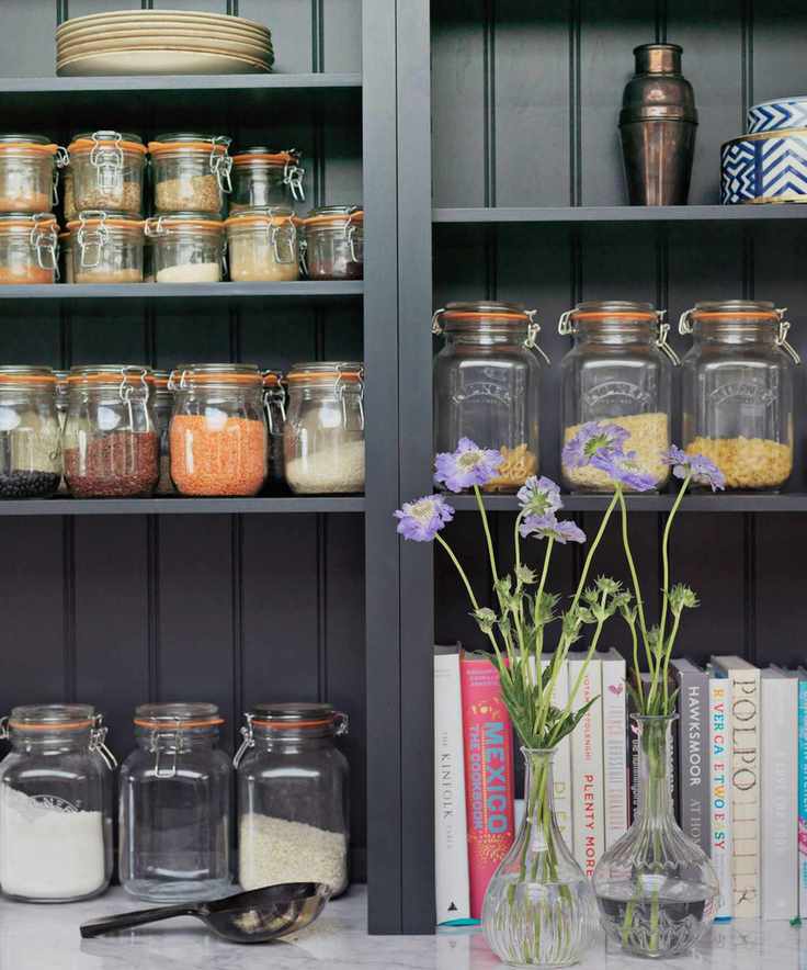 A pantry with black shelving, glass food storage jars, recipe books and two glass vases filled with purple flowers.