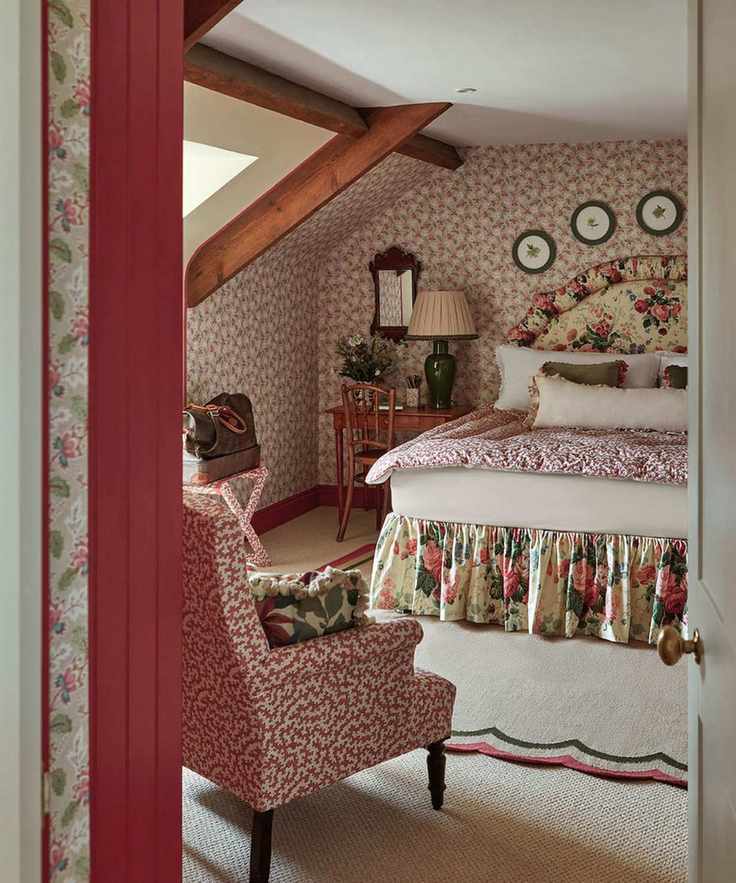 attic wallpapered bedroom with a low beamed ceiling and a floral headboard with matching bed skirt sat on a scalloped rug