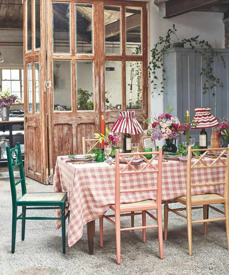 Garden room table setup with gingham table cloth, green glassware, wine bottle lamps and a rustic doorway in the background