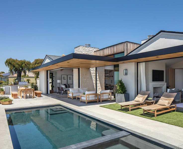 A pool area with sun loungers and an outdoor living space with a roof cover