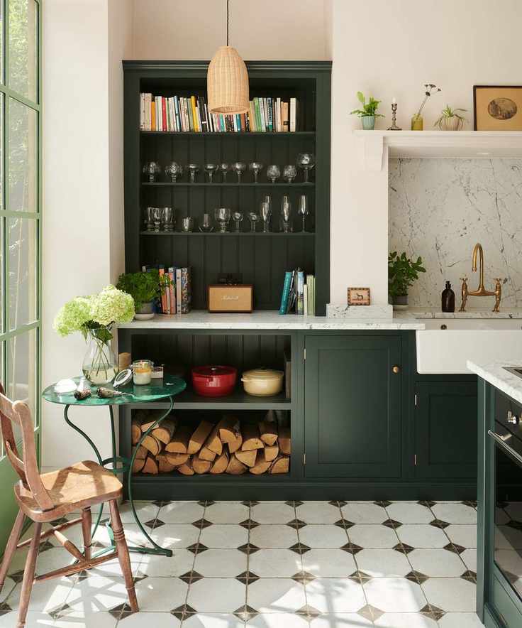 dark green kitchen with a full height open cabinet shelving unit with displays of cookbooks, glassware, le creuset dishes and chopped wood