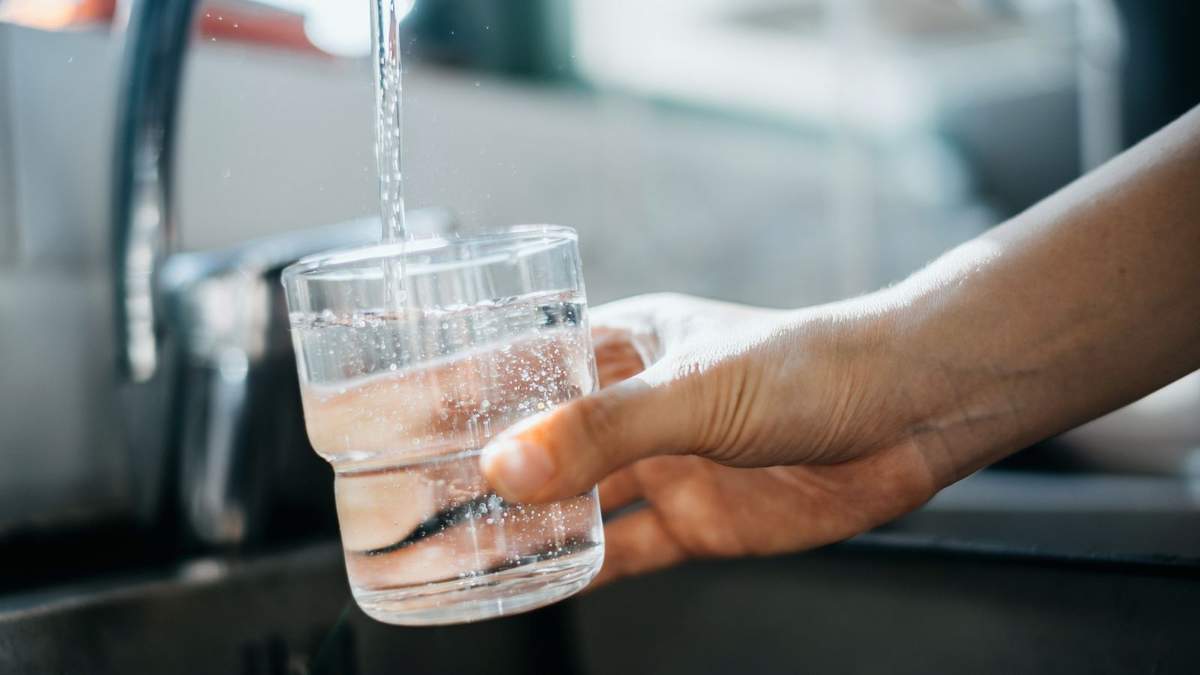 A hand holding a glass of water under the tap