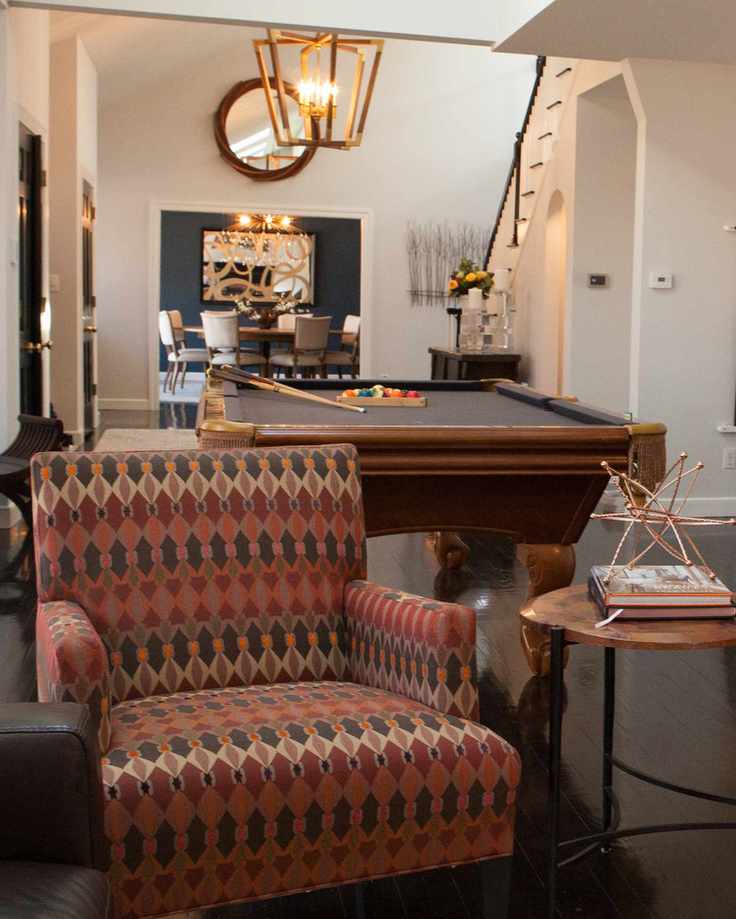 living area with pool table, upholstered armchair, side table with ornament, dining room in background, staircase, large pendant light, hardwood floor