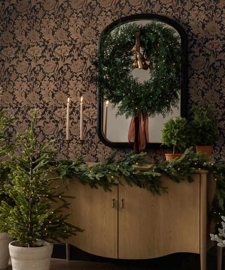 christmas garland on cabinet with wreath displayed on mirror and small potted christmas tree