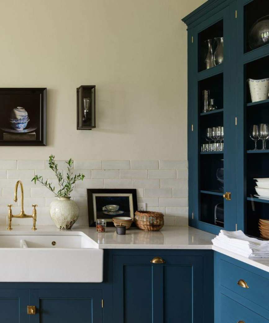 A kitchen with blue cabinetry with brass handles, white walls and work surfaces
