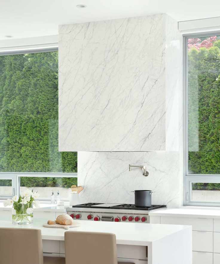 Chic white kitchen featuring a large white marble hood