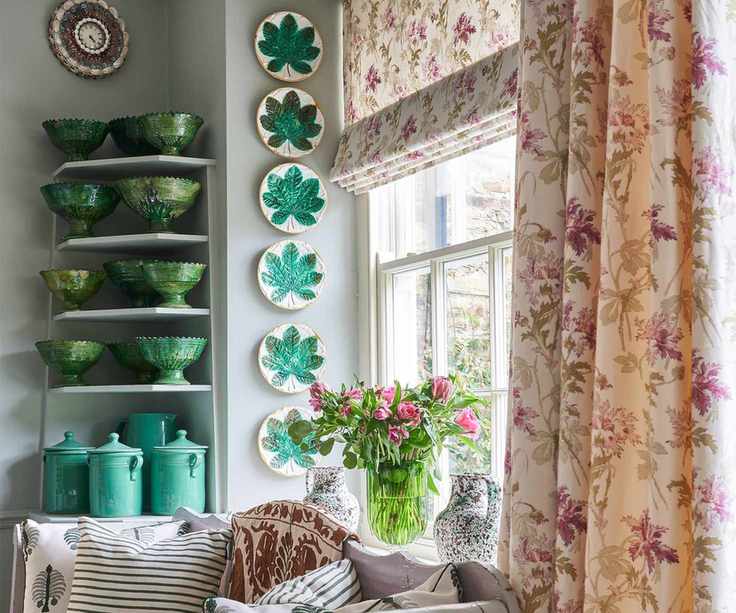 Green ceramics on shelf with plates on wall and day bed and large window with patterned curtains