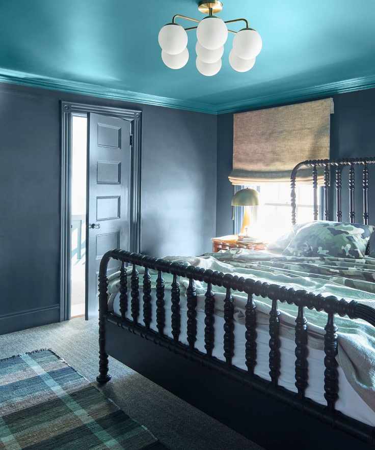 Bedroom with bright blue ceiling, dark blue walls, bobbin frame bed, plaid rug, blue patterned bedding, gold lamp