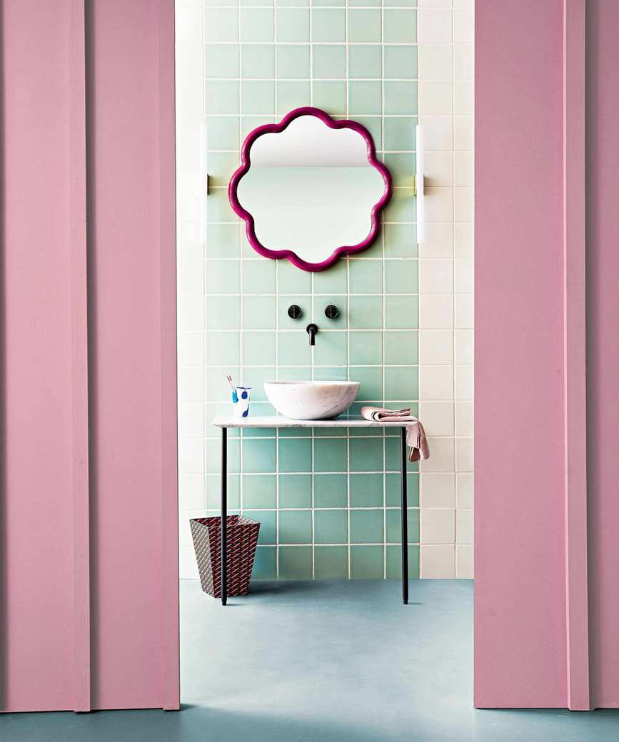 Pink and blue bathroom, pink painted walls with blue and white tiles and pink scalloped mirror above sink