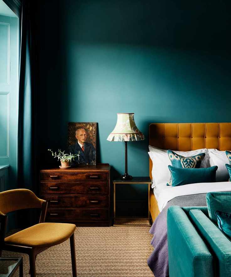 A cozy bedroom featuring teal walls, mustard bedding, and wooden furnishings.