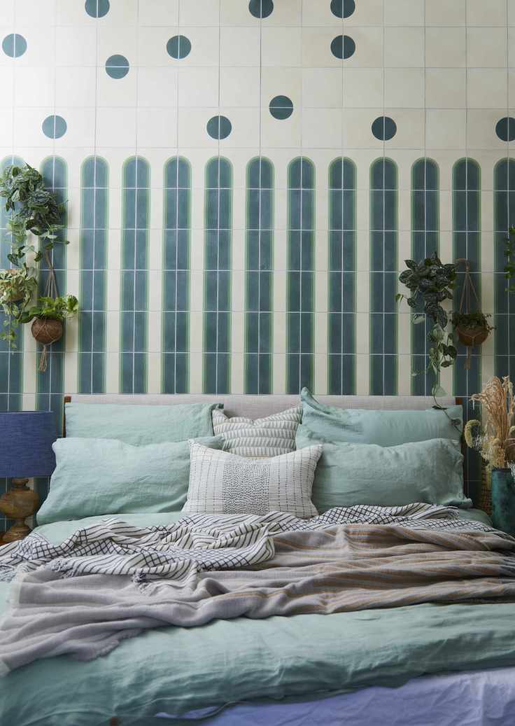 green bedroom with green bedding, tiled background behind bed, blue lamp, plants