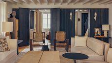 a rustic living room in a french home with ceiling beams, neutral sofas and navy woodwork