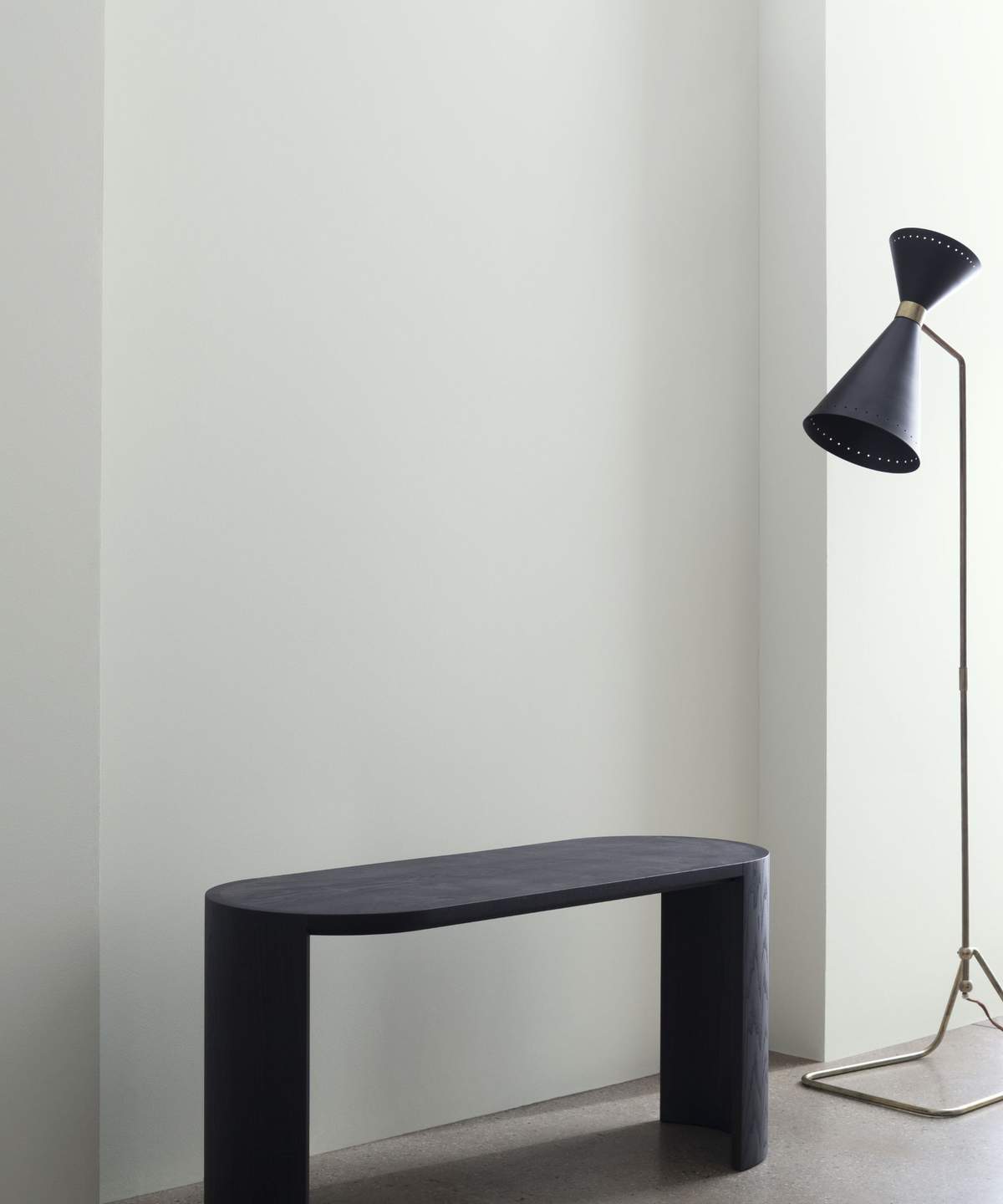 A room with a black floor lamp and black bench, the wall painted in a creamy gray.