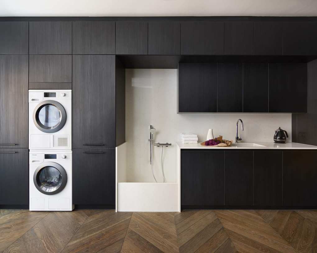 Wall to ceiling laundry room storage ideas with black wood ceiling height cabinets and stacked appliances.