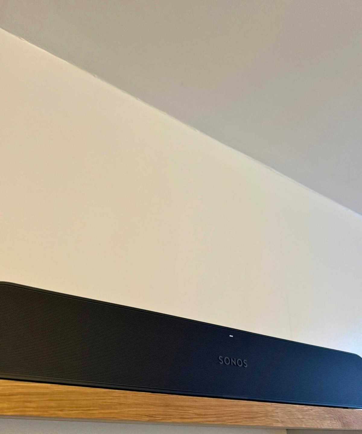 The Sonos Ray soundbar on a wooden shelf in front of cream-white wall.