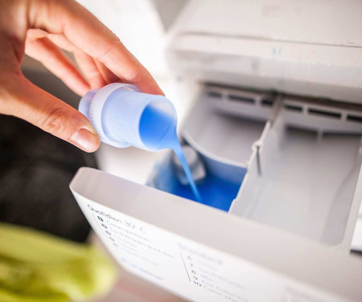 Someone pouring liquid laundry detergent into a cap