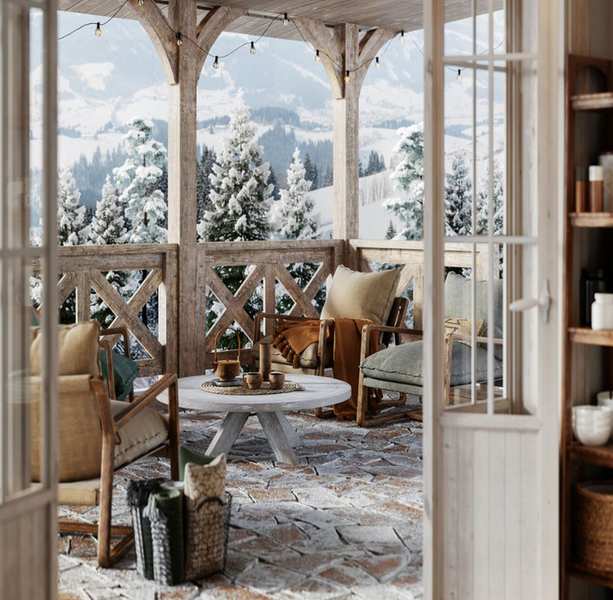 An outdoor patio with armchairs and a table with tea cups on it, with string lights on the wooden canopy and snowy trees in the distance