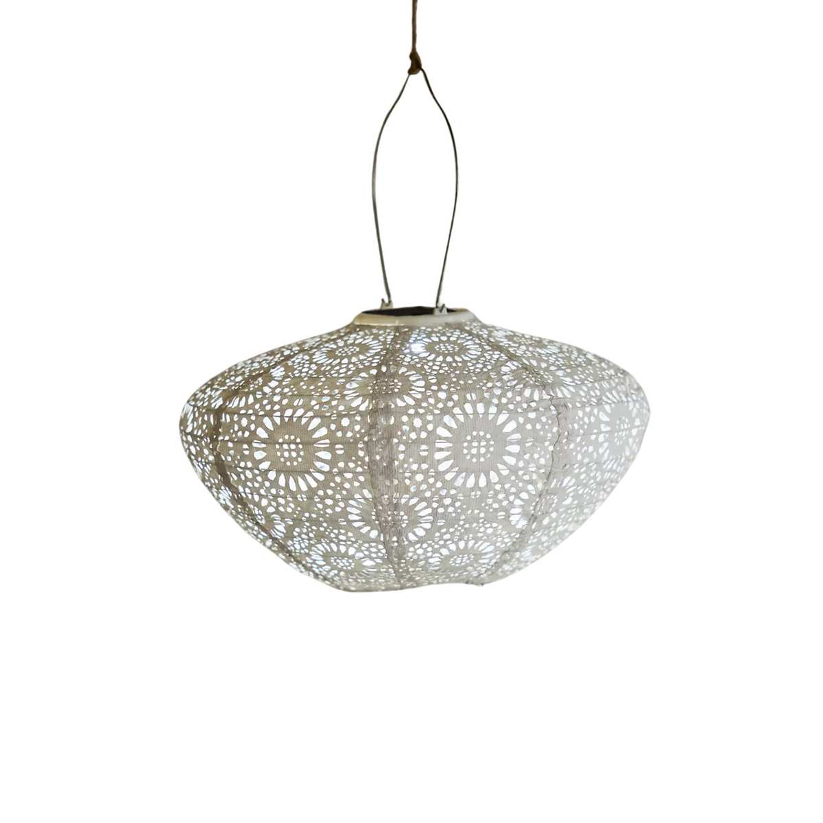 A white solar lantern with a lace pattern, hanging from a wire