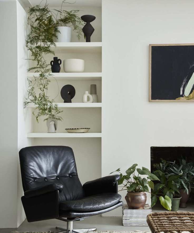 corner of living room with white walls with shelving, black leather swivel chair, lots of plants