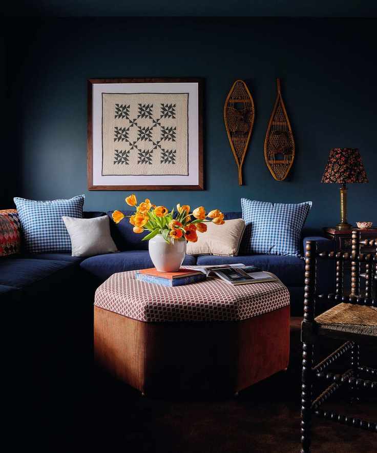a media room painted navy with a navy couch and plaid pillows, a patchwork piece of art, rattan decor, ottoman and bobbin chair