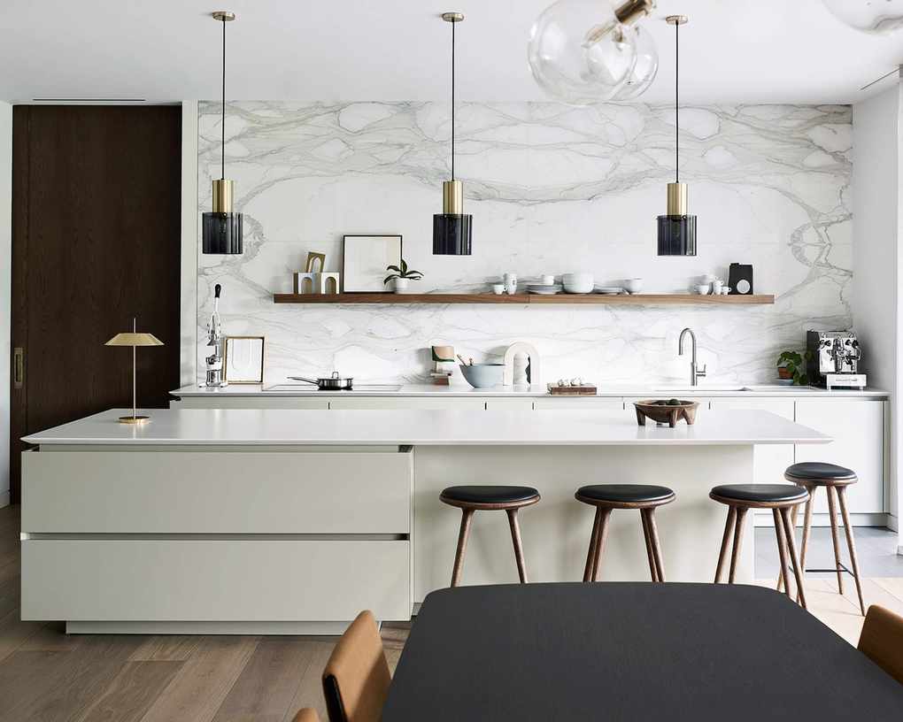 Chic white kitchen with an island featuring handleless drawers and a large marble backsplash