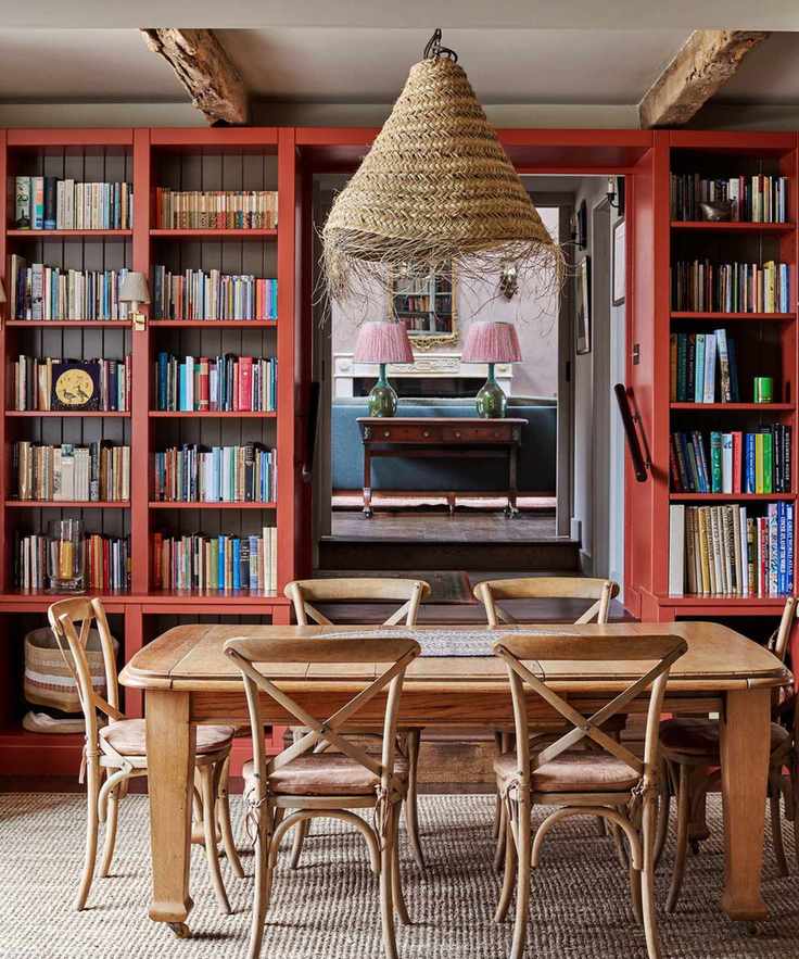 A dining room with red colorful bookshelves, a wooden dining table with chairs, and a woven pendant lamp.