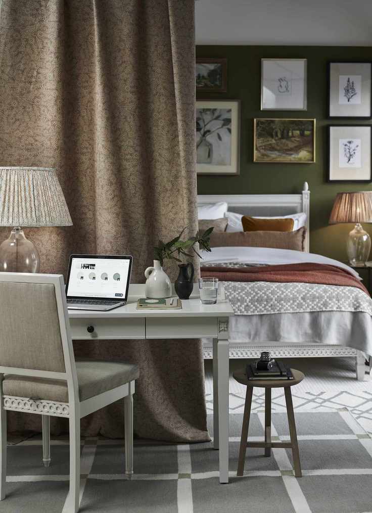 bedroom home office, green walls, curtain, white desk and chair, white painted bed, gallery wall, rugs, glass based table lamp