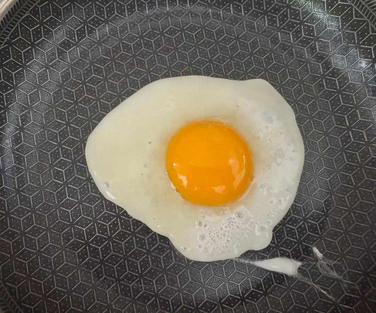 Fried egg, sunny side up, in a black lined frying pan.