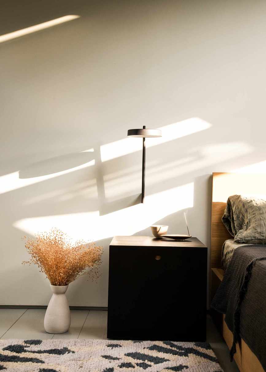 A Mid-Century Modern style bedroom with a wooden bedframe, a dark black nightstand, and a structural lamp sconce on the wall