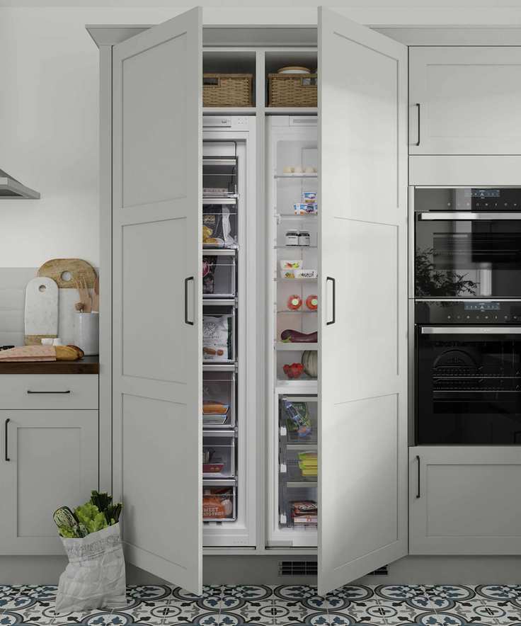Integrated floor to ceiling fridge and freezer, with the doors open, in a very pale green kitchen with geometric blue and green tile floor