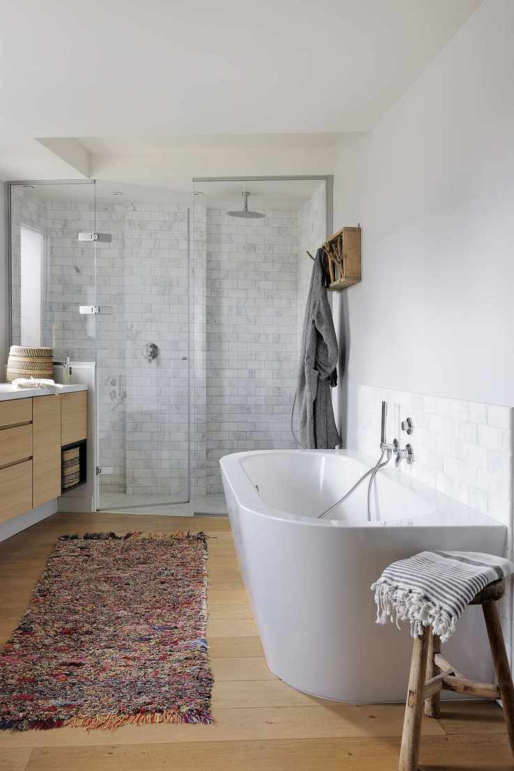 bathroom with wooden floorboards, rug, white tub, walk in shower at one end, bathroom cabinet, stool, hanging unit