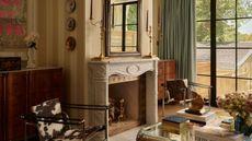 a Toronto living room with yellow striped walls, a large window dressed with light green drapes, antique marble fireplace, a cow print chair and vintage furniture