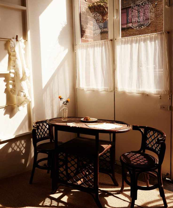 corner of a kitchen with muted pink walls and a bistro set of chairs with cafe style curtains