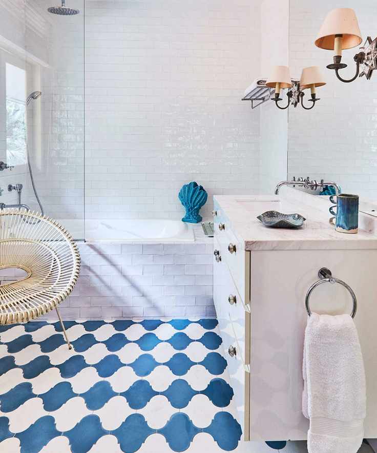 A white tiled bathroom with blue and white tiled flooring, a tiled bathtub, and a white cabinet with a white marble countertop and large mirror.
