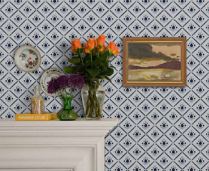 How to wallpaper, with a diamond print blue and white design hung above a fireplace, with plates and a painting mounted on the wall.