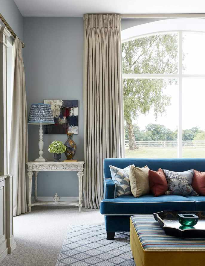 living room with blue couch, cream drapes, console, table lamps, patterned cushions, footstool
