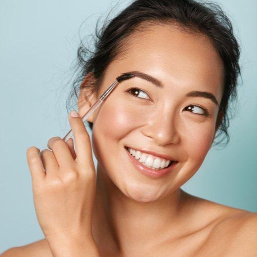 Woman applying moisturizer to eyebrows with a spoolie