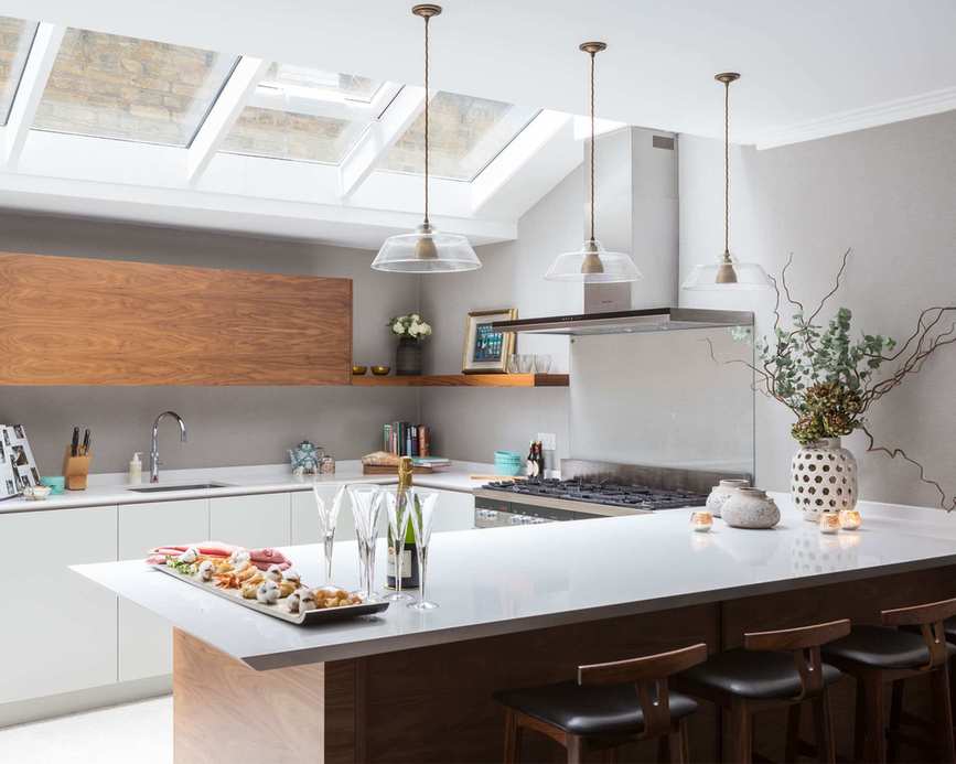 White kitchen, quartz worktops, large island unit with breakfast bar, wooden details, three glass pendant lights hanging over counter