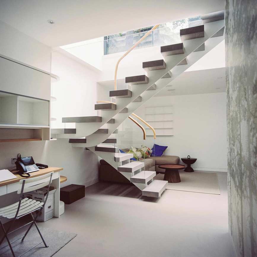 Open tread staircase with glass balustrade leading to basement with neutral decor with seating area and desk